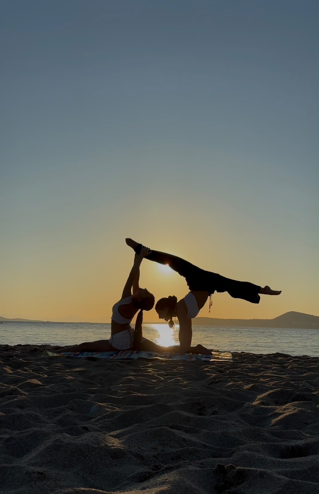 Partner yoga pose on the beach at sunset